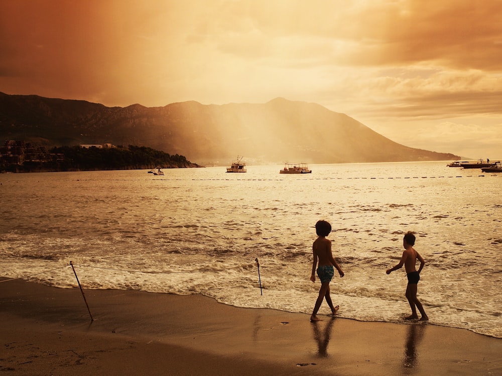 duas crianças caminhando na praia durante o pôr do sol