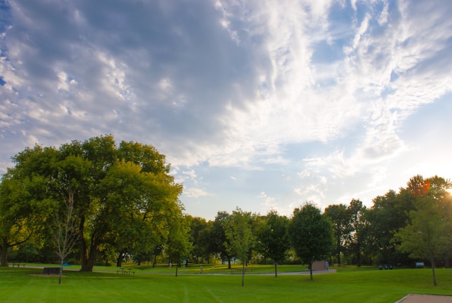A panoramic view of a landscaped park with green lawns and shaded benches.