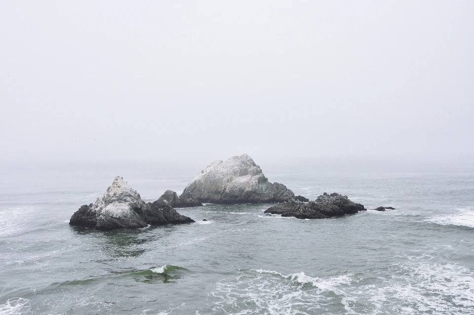 Three large rocks jut out from the water's surface, surrounded by smaller ones nearby