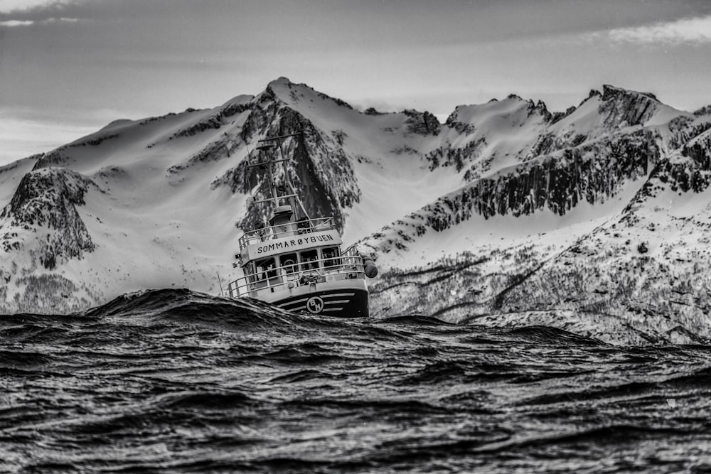 grayscale photography of ship on body of water near at snowy mountain