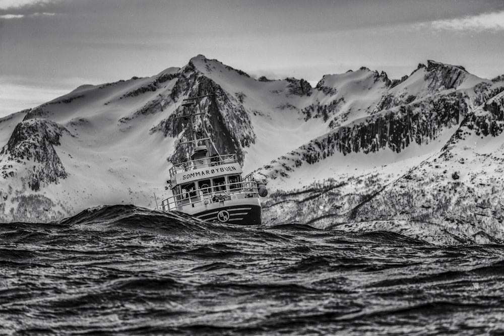 Fotografía en escala de grises de un barco en un cuerpo de agua cerca de la montaña nevada