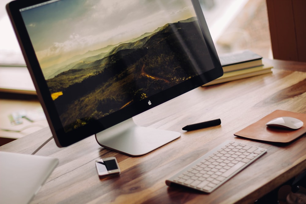 iMac grigio siderale vicino alla Magic Keyboard sulla scrivania del computer in legno marrone durante il giorno