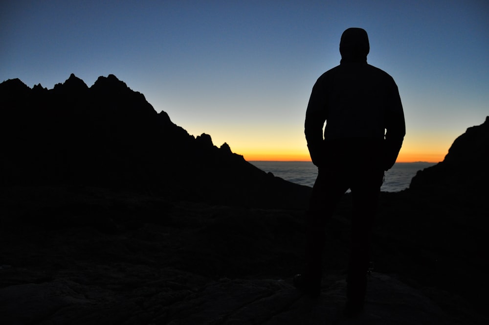 Silhouette de personne au sommet de la montagne sous le ciel bleu pendant le coucher du soleil orange