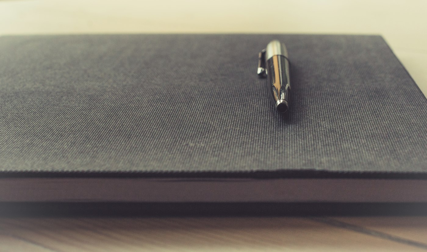 A pen resting on a closed dark notebook