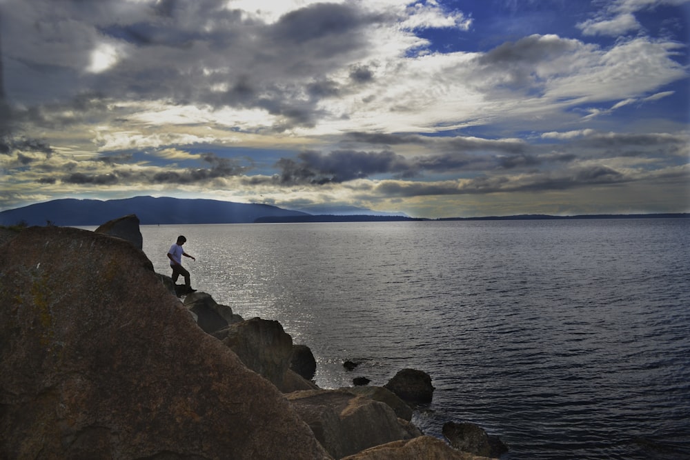 person standing on rocky cliff near body of water