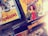 A collection of comic books is displayed, with covers featuring colorful illustrations. One prominent cover shows a woman in a red dress, accompanied by various characters and an amusement park ride in the background. Another comic cover displays a dynamic scene with a construction vehicle and workers.