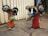 Two whimsical sculptures resembling mice are crafted from scrap metal and painted in bright colors. They have exaggerated features like large ears and eyes made from recycled parts. The sculptures are standing on a stone pavement, and there is a sign in the background indicating a sale.