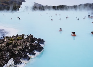 people swimming on hot spring near mountain during daytime