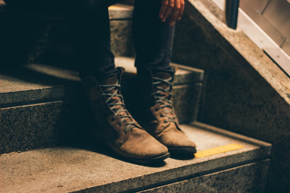 person wearing pair of brown lace-up boots with sitting on stairs