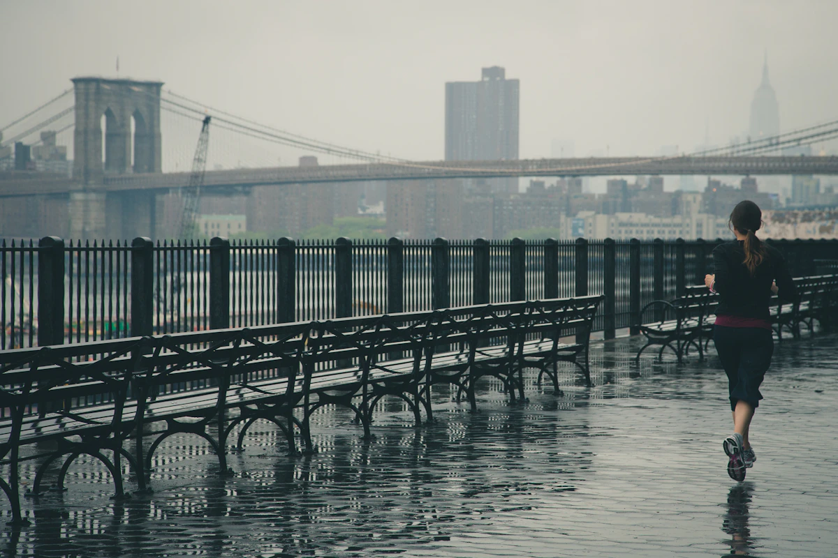 A woman running steadily beside the water in light rain
