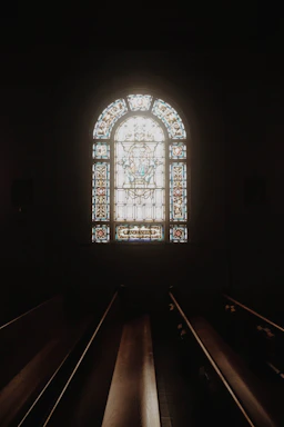 A peaceful church interior with soft sunlight streaming through stained glass windows.