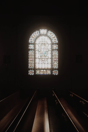 The interior of the chapel with soft light filtering through stained glass, highlighting wooden pews.