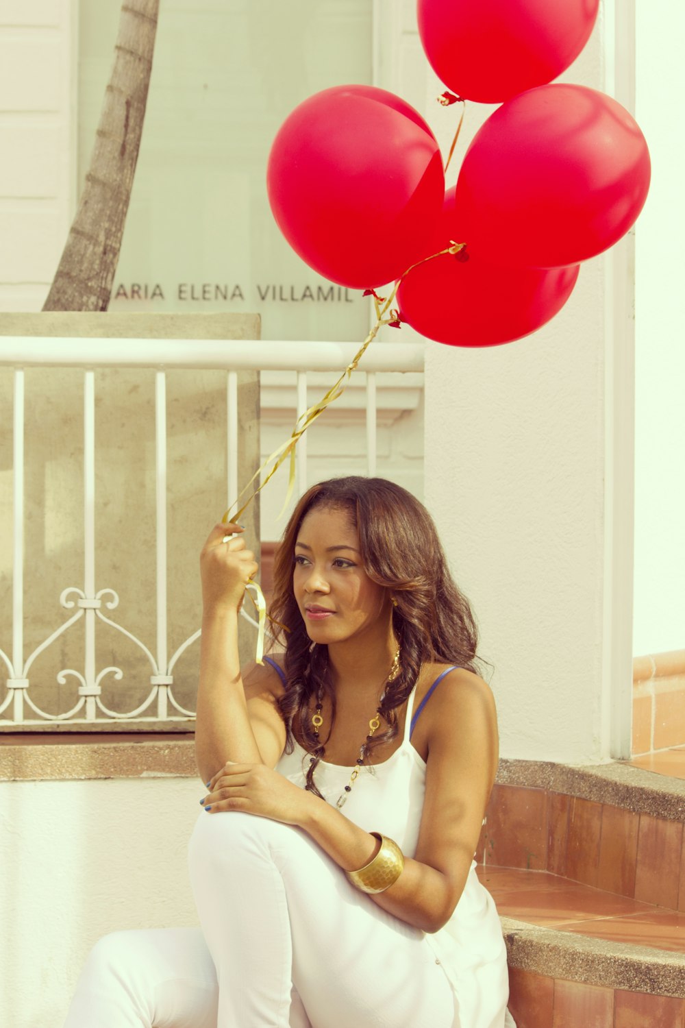 woman sitting on staircase while holding red balloons