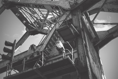 An industrial structure with metal beams and riveted joints, showcasing intricate latticework and towering framework against a partly cloudy sky.