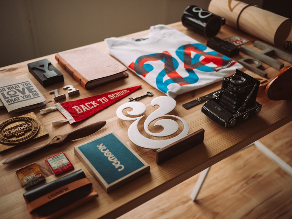 A flatlay with a t-shirt, a camera, a notebook and various trinkets on a table