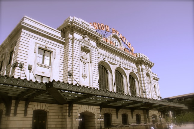 A historic train station with a grand architectural facade featuring large arched windows and ornate detailing. The building has a prominent sign with 'Union Station' displayed at the top.