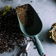 green metal garden shovel filled with brown soil