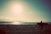 Person carrying a crepuson speaker on a surfboard at dusk, ready for an evening by the waves.