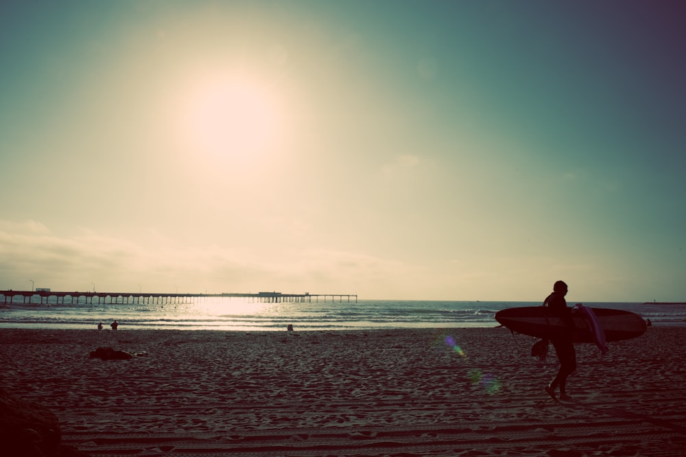 persona che trasporta tavola da surf vicino alla riva del mare