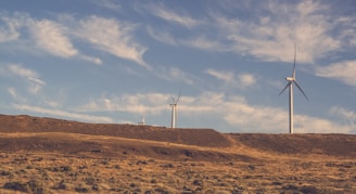 two gray wind turbines under cloudy blue sky during daytime