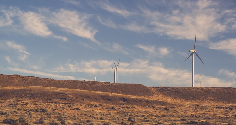 two gray wind turbines under cloudy blue sky during daytime