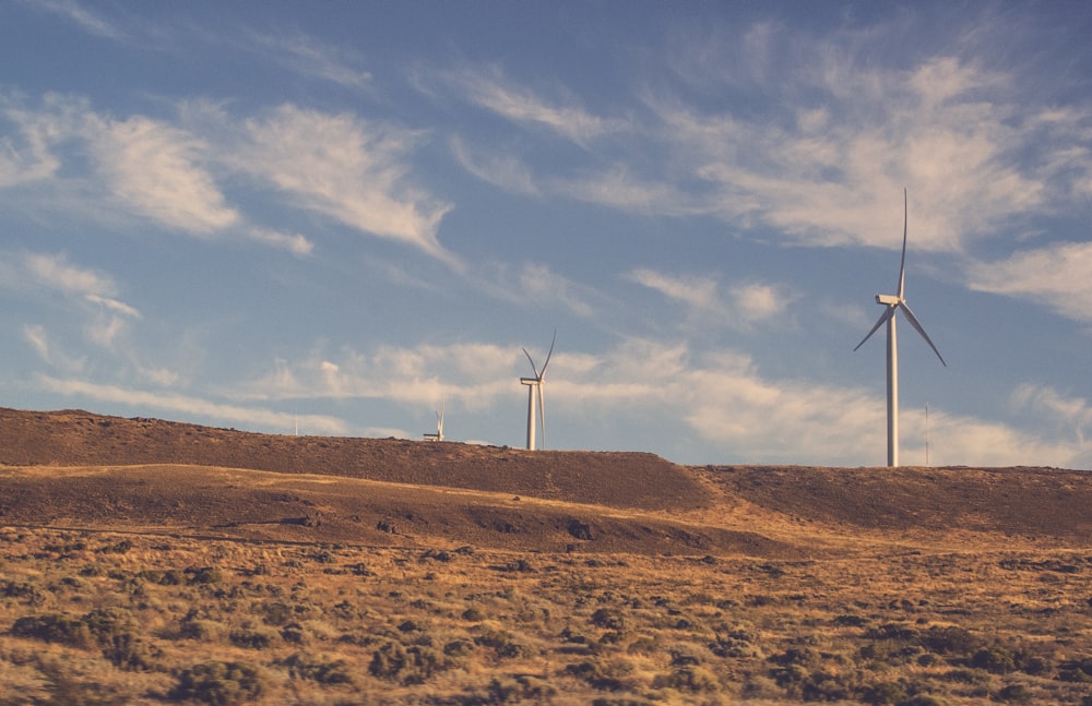 Zwei graue Windräder unter bewölktem blauem Himmel bei Tag