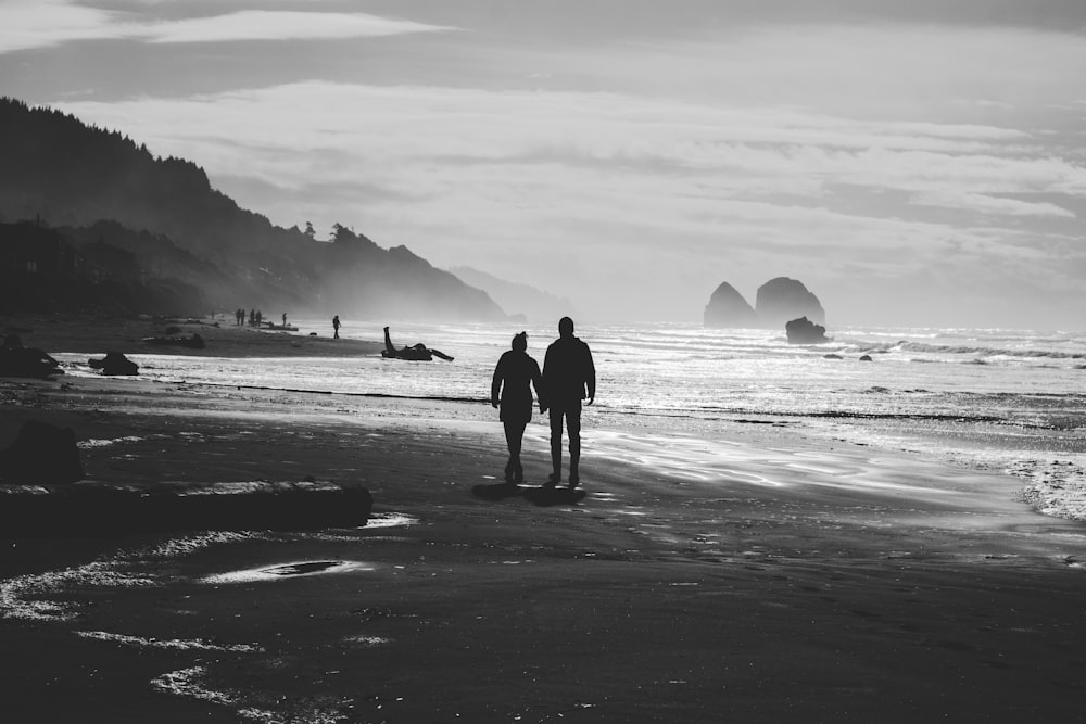 grayscale photo of man and woman walking on seashore