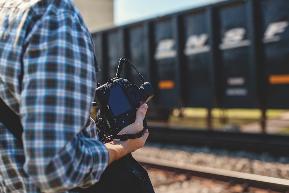 person holding DSLR camera near cargo container during daytime