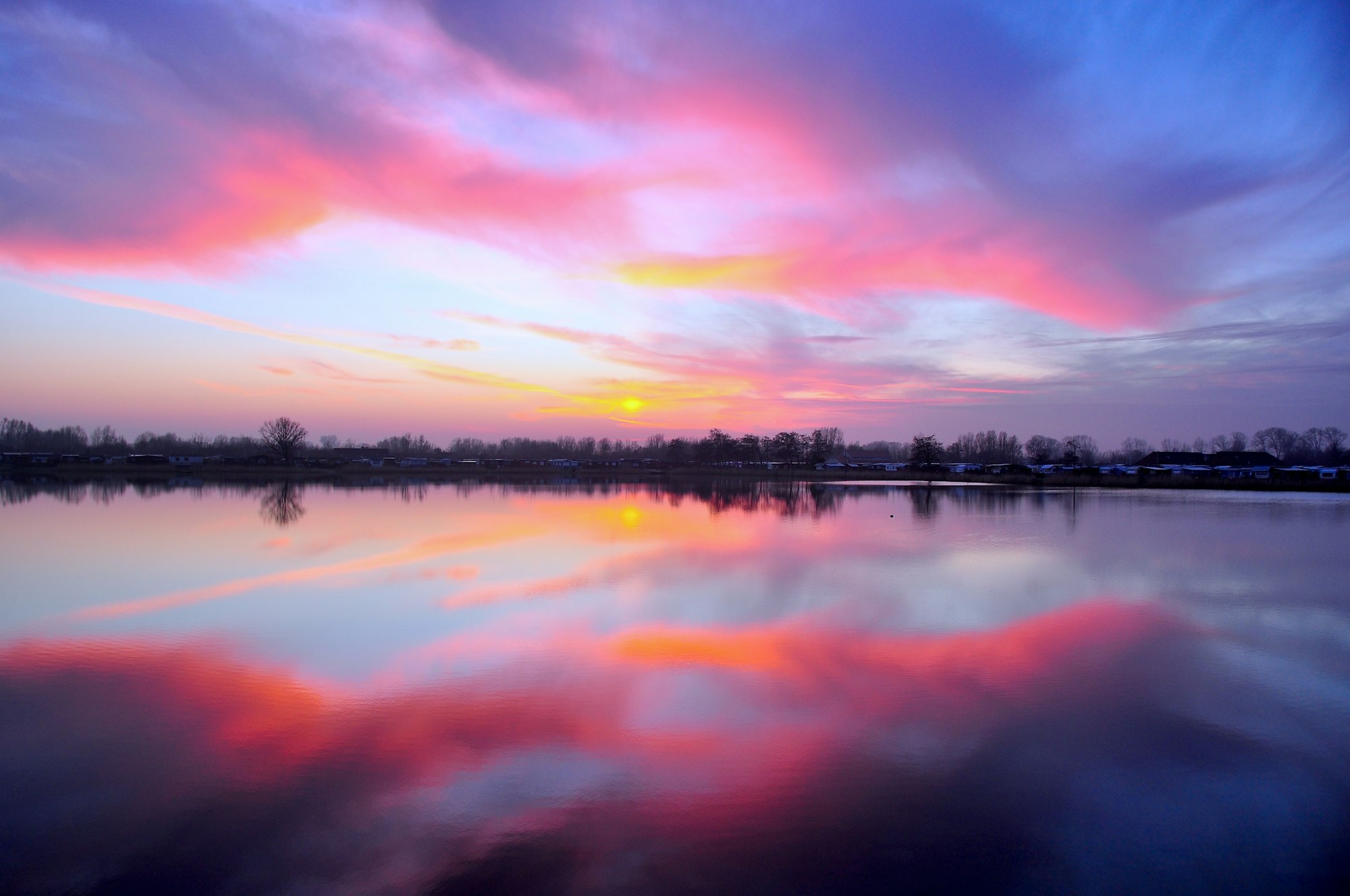 an orange and pink sunrise over a lake with trees on the shoreline in the background