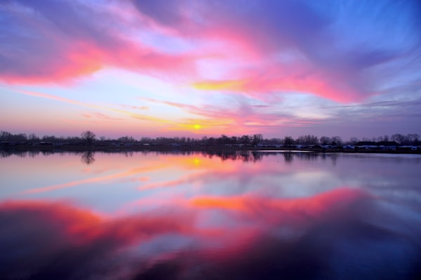 an orange and pink sunrise over a lake with trees on the shoreline in the background