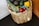 A woven basket filled with fresh produce including avocados, asparagus, grape tomatoes, and a yellow bell pepper. The produce is arranged neatly, highlighting their vibrant colors against the natural tones of the basket.