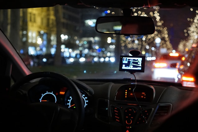 A sleek navy blue and silver GPS tracking device mounted inside a car dashboard, glowing softly against a city skyline at dusk.