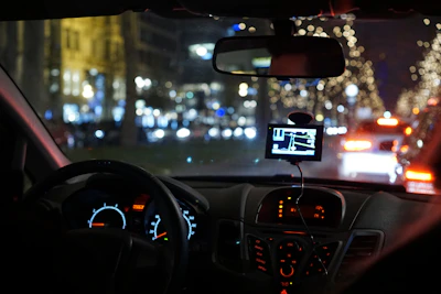 A GPS tracker device glowing on a car dashboard at dusk.