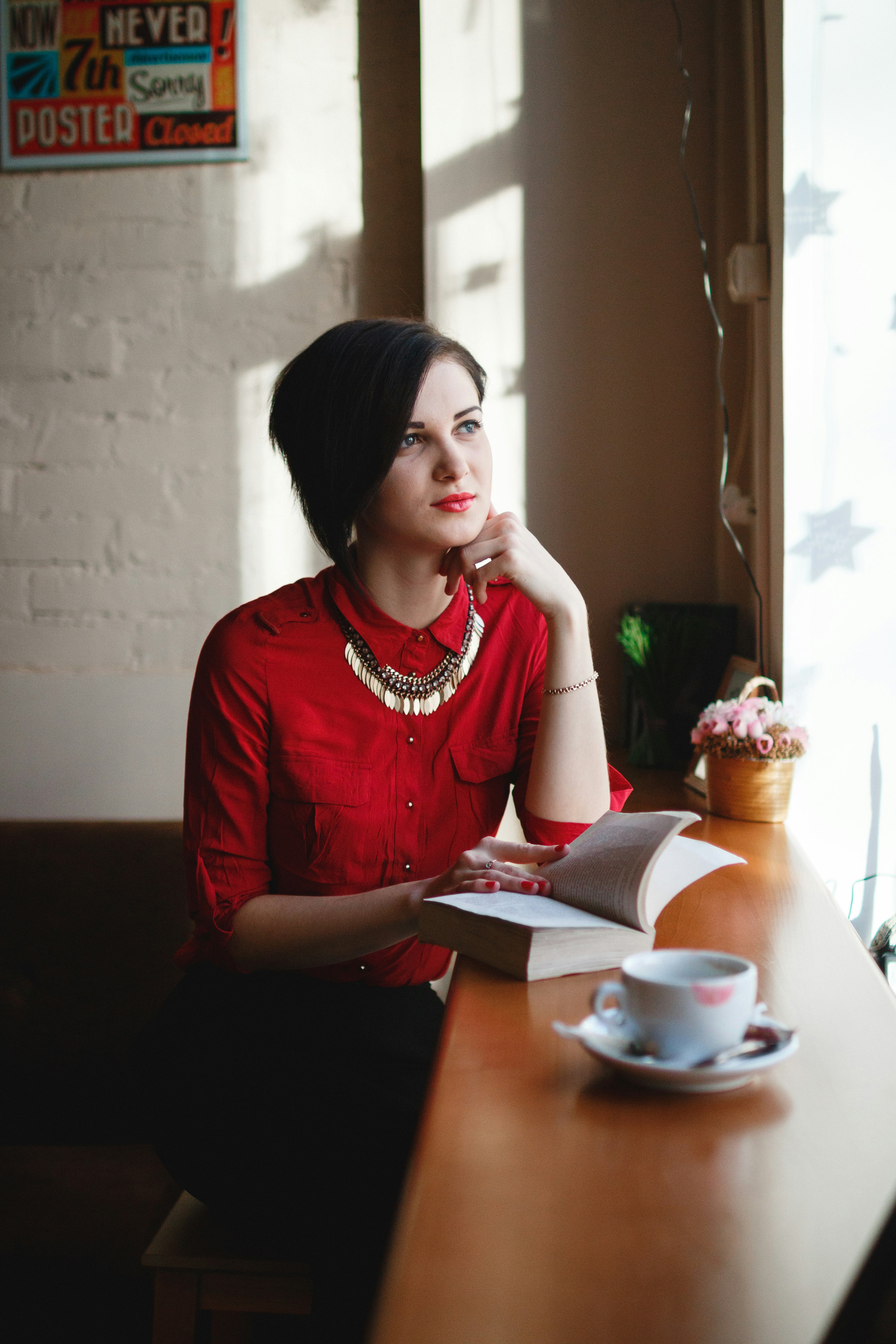 woman leaning on brown wooden table while holding book