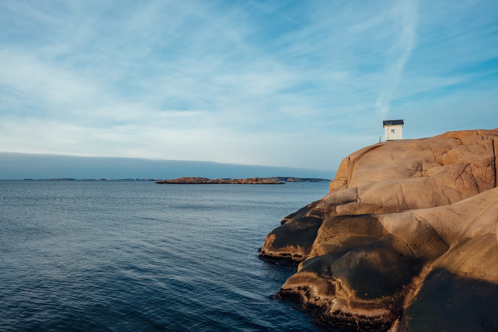 Maison en béton blanc sur une formation rocheuse près de la mer pendant la journée