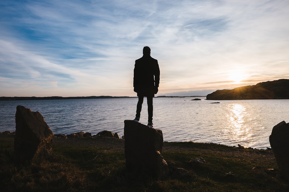 person standing on rock facing ocean