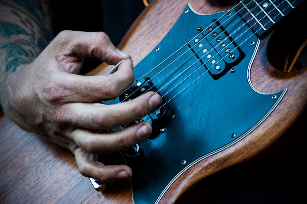 person plucking electric guitar with guitar pick