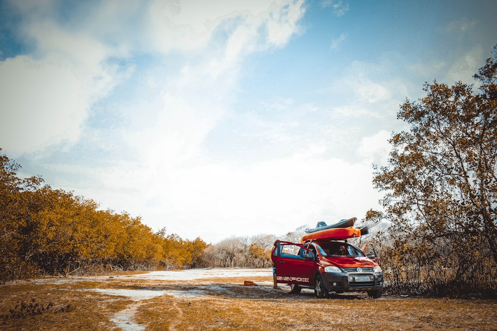 red vehicle on dirt road near trees at daytime