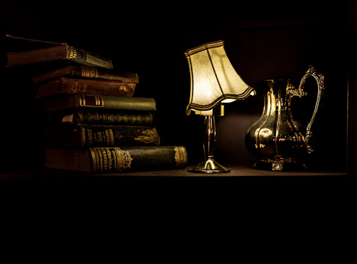 turned on desk lamp beside pile of books