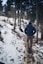 man wearing black hooded coat walking under trees with snow during winter