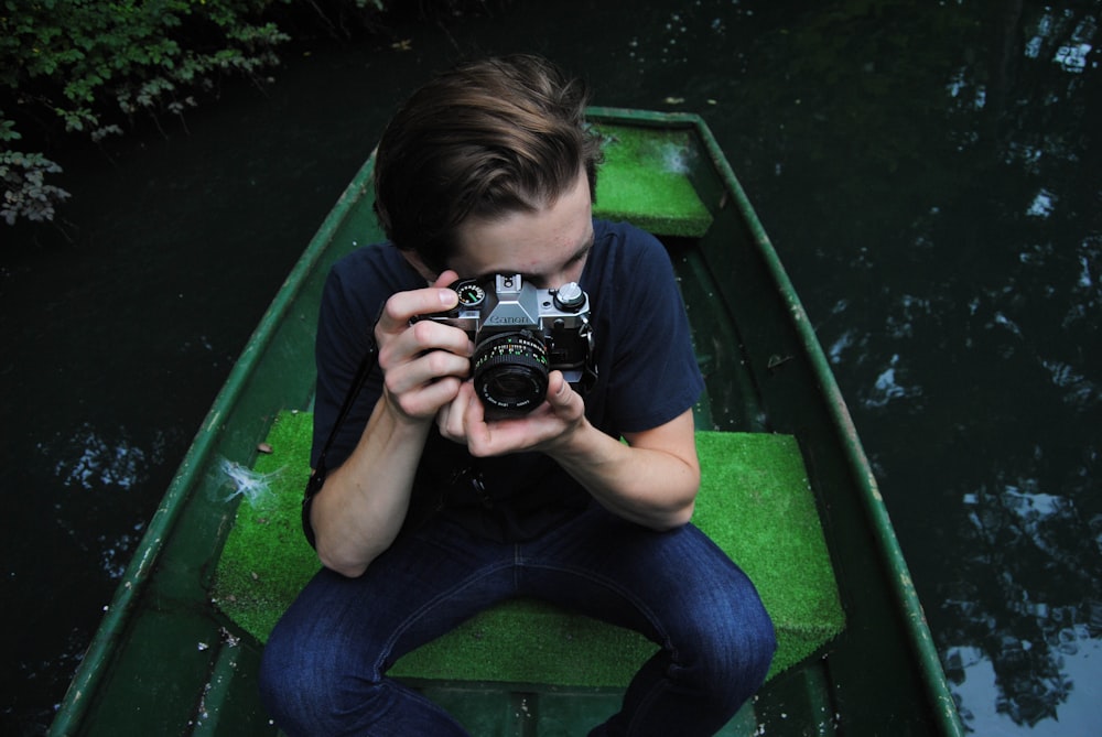 Mann in schwarzem T-Shirt und blauen Jeans fährt auf Ruderboot und hält Brückenkamera auf Fokusfoto