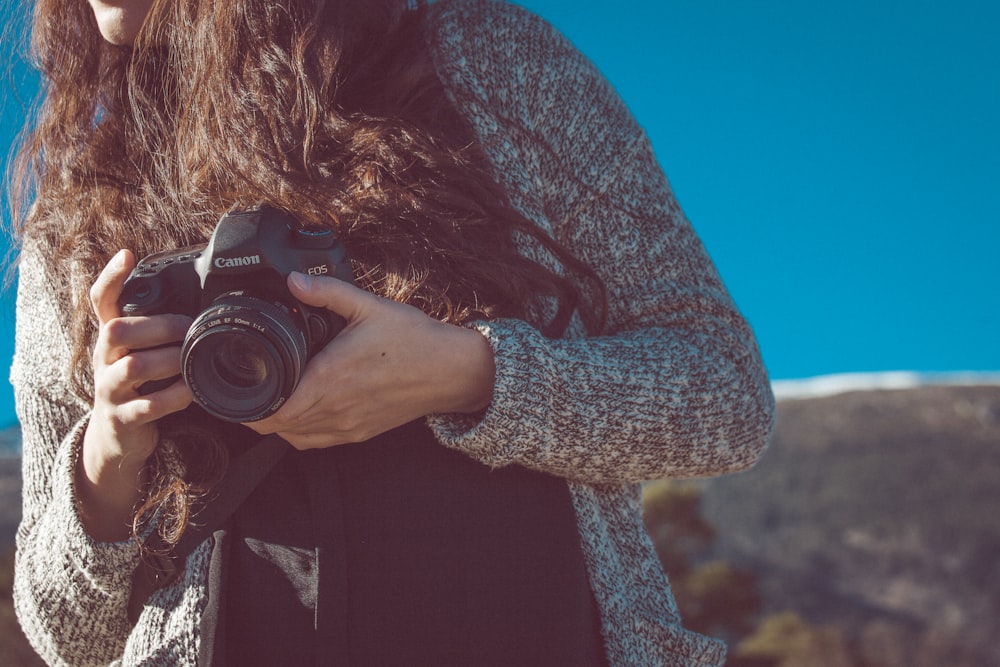 검은 캐논 DSLR 카메라를 들고 있는 여자