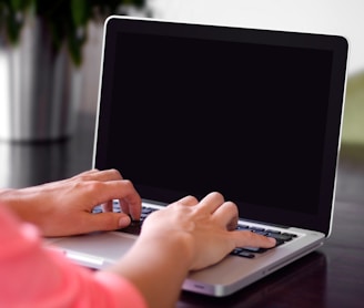 person wearing pink shirt typing on gray laptop computer on desk