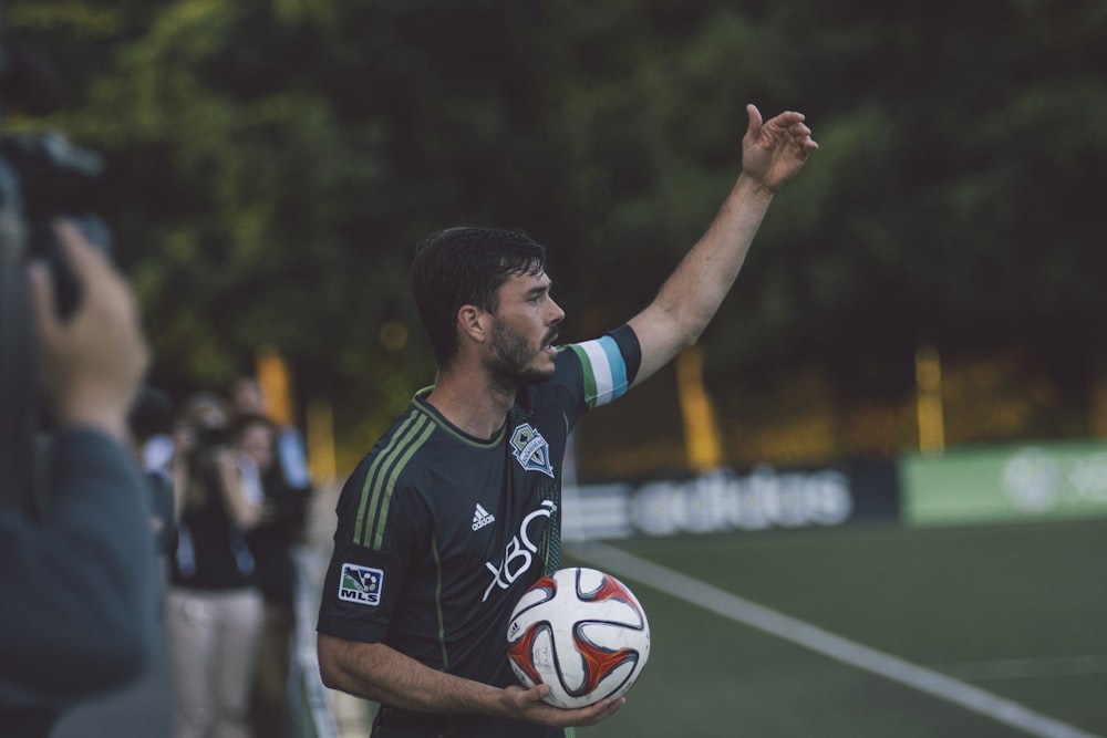 man in black and green Adidas jersey shirt holding soccer ball