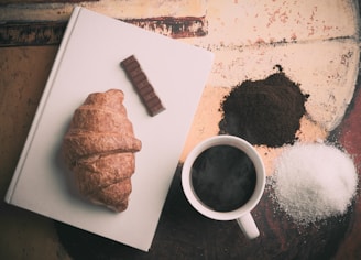 bread on white book beside ceramic mug