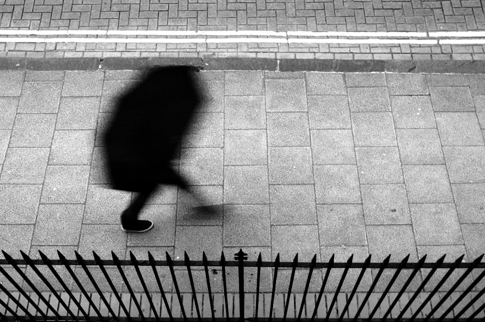 a person walking down a sidewalk next to a fence