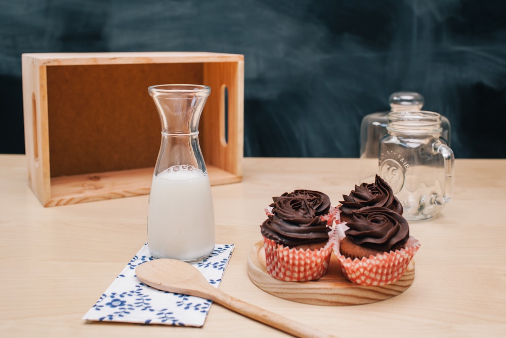 quatre cupcakes sur un sous-verre brun et un pot de lait