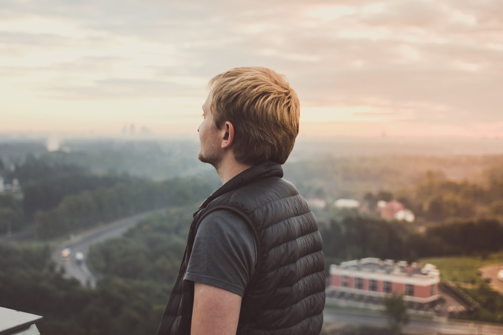 A man in a vest looking into the distance over a landscape of trees and buildings