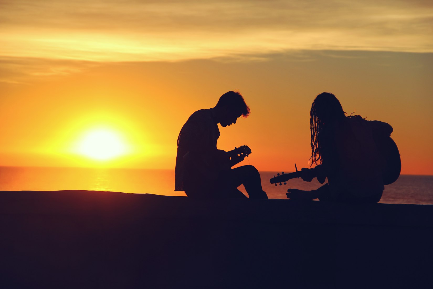 Two people with guitars in front of a sunset