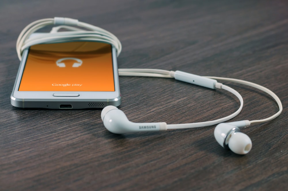 white Samsung Android smartphone turned beside white earbuds on brown board